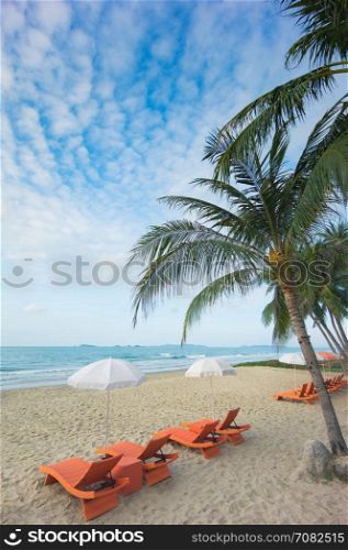Orange beach chairs and parasols on sandy beach with cloudy blue sky and sea