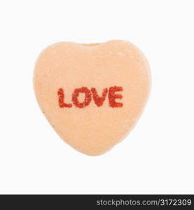 Orange candy heart that reads love against white background.