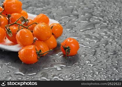 Orange cherry tomatoes in water drops on a gray table. Dark style, close-up with copy space. Ingredients for salad or dish with vegetables. selective focus