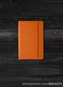 Orange closed notebook mockup isolated on black wood background. Orange closed notebook on black wood background