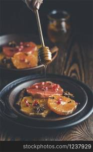 Orange dessert with wine honey or maple syrup and ginger spice, decorated pomegranate berries. Wonderfully sweet, rich and fresh food. Dark rustic background, copy space for you text.