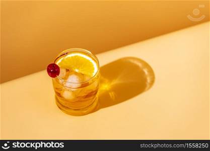 Orange drink cocktail with slice orange and cherry in glass with water drops on yellow background in bright sun light. Copy space, summer vacation and party concept