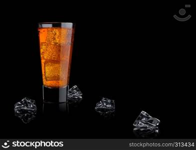 Orange energy soda drink glass with ice cubes on black background