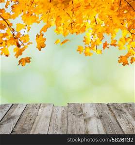 Orange fall leaves over wooden desk and abstract autumn background