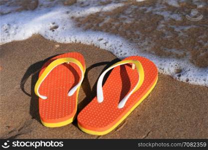 Orange flip-flops in sand on the beach in Barcelona.
