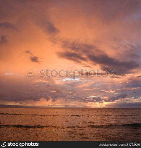 Orange glowing clouds during sunset on coast in Maui Hawaii.