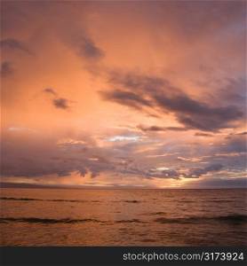 Orange glowing clouds during sunset on coast in Maui Hawaii.