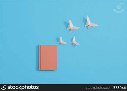 Orange hardcover notebook lying flat on a pastel blue background with origami butterflies coming out of notebook. Copy space and room for text