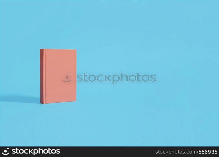 Orange hardcover notebook standing on a pastel blue background. Left composition on a horizontal image with space for copy and text.