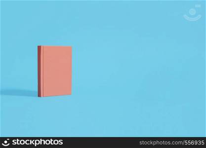 Orange hardcover notebook standing on a pastel blue background. Left composition on a horizontal image with space for copy and text.