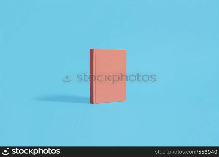Orange hardcover notebook standing on a pastel blue background. Center composition with space for copy and text
