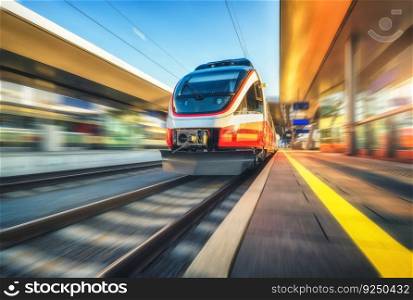 Orange high speed train in motion on the railway station at sunset. Fast moving modern intercity train and blurred background. Railway platform. Railroad in Austria. Passenger transportation. Concept	
