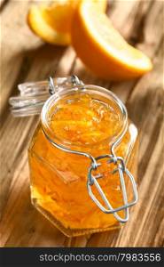 Orange jam in swing-top jar on wood with orange slices in the back, photographed with natural light (Selective Focus, Focus on the first two orange peels on the jam)