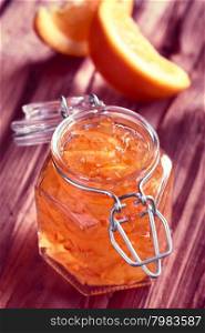 Orange jam in swing-top jar on wood with orange slices in the back, photographed with natural light (Selective Focus, Focus on the first two orange peels on the jam) (Digitally Altered: Toned Image)