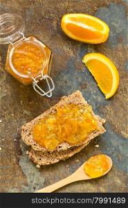 Orange jam on wholegrain bread slices, photographed overhead on slate with natural light (Selective Focus, Focus on the orange jam on the bread)