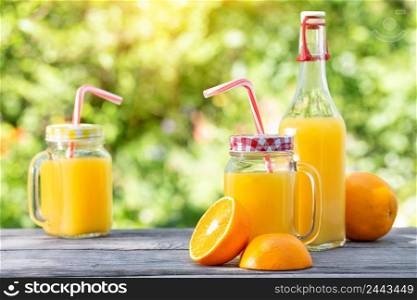 Orange juice and sliced oranges on a wooden table. Natural green background. Orange juice and sliced oranges on a wooden table