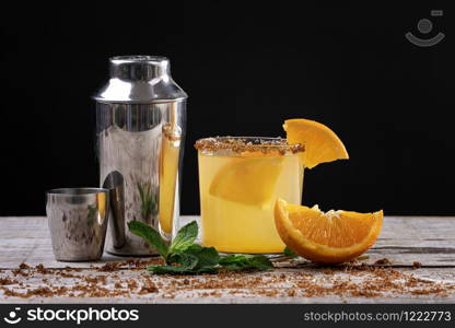 orange juice cocktail on a wooden base decorated with a metal shaker