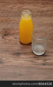 Orange juice in a bottle with an empty glass isolated against a wooden background