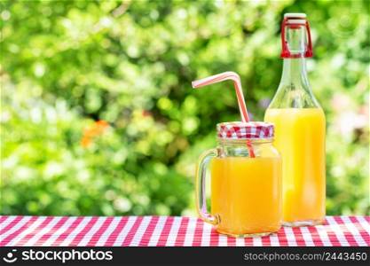 Orange juice in mason jars and bottle on wooden table. Natural green background.. Orange juice in mason jars and bottle on wooden table