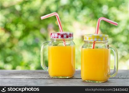 Orange juice in mason jars with straws on a wooden table. Natural green background. Orange juice in mason jars with straws on wooden table