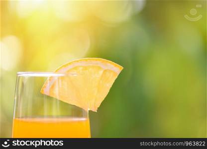 Orange juice with piece orange fruit on glass with nature green summer background - selective focus