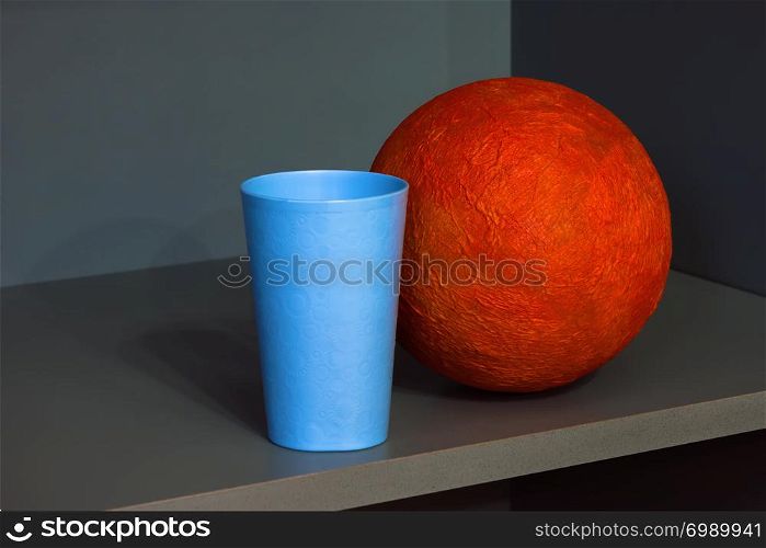 Orange papier-mache ball and blue plastic cup in the corner of the shelf - abstract geometric design.. Abstract Composition With Orange Sphere