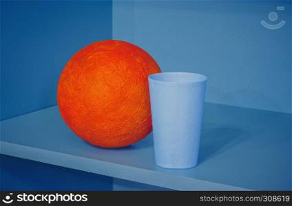 Orange papier-mache ball and plastic cup in the corner of the blue shelf - abstract geometric design with space for copy.. Abstract Composition With Orange Ball
