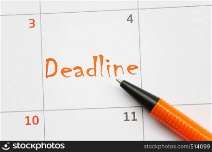 Orange pen that points to a deadline text on calendar background.