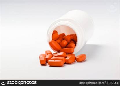 orange pills spilling from bottle on grey background