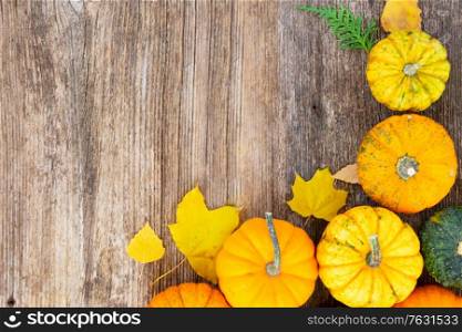 orange raw pumpkins on old wooden textured table with fall leaves close up, top view border. pumpkin on table