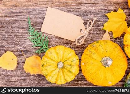 orange raw pumpkins with leaves on old wooden textured table, top view with copy space on paper tag, retro toned. pumpkin on table