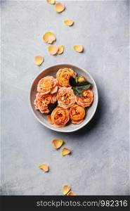 Orange roses floating in water on concrete background, SPA and relaxation concept, flat lay
