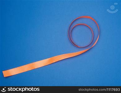 orange silk thin ribbon twisted on a blue background, trendy blue color, top view