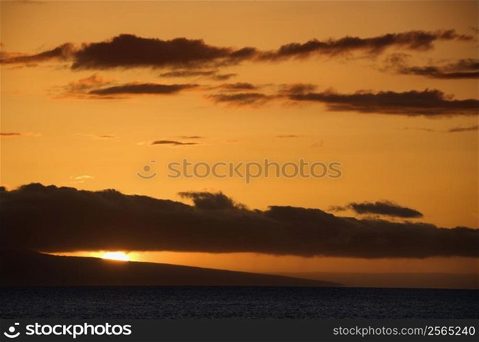 Orange sunset behind island in Pacific ocean.