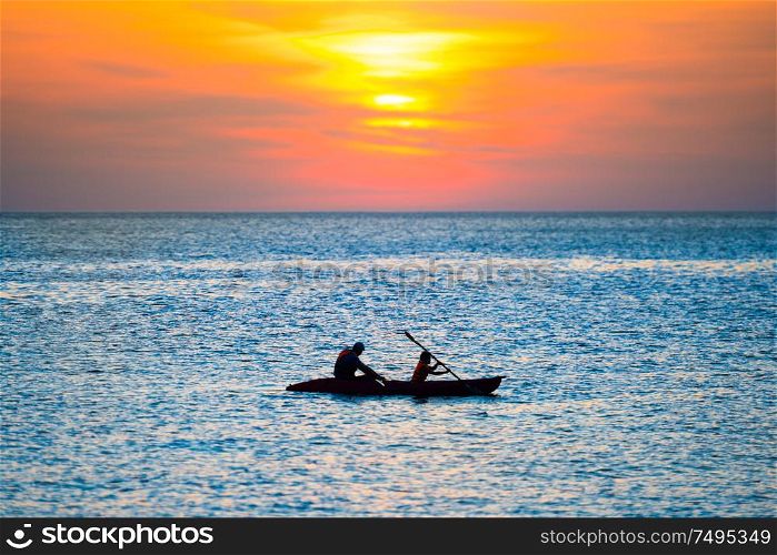Orange sunset over blue sea and silhouette of kayak in rippled water
