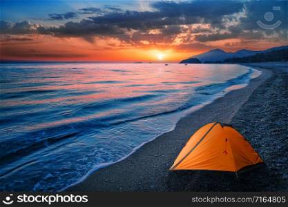 Orange tent by the sea or ocean on a background of mountains. Dramatic sunset sky. Orange tent by sea or ocean on background of mountains