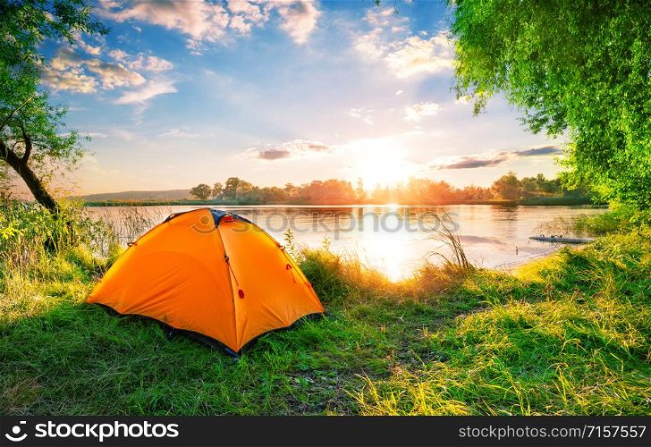 Orange tent on the lake at sunset. Bright sun. Summer landscape. Orange tent on the lake at sunset