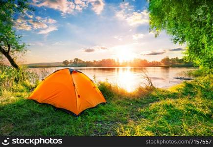 Orange tent on the lake at sunset. Bright sun. Summer landscape. Orange tent on the lake at sunset