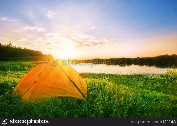 Orange tent on the river bank at sunset in summer. Orange tent on the river bank