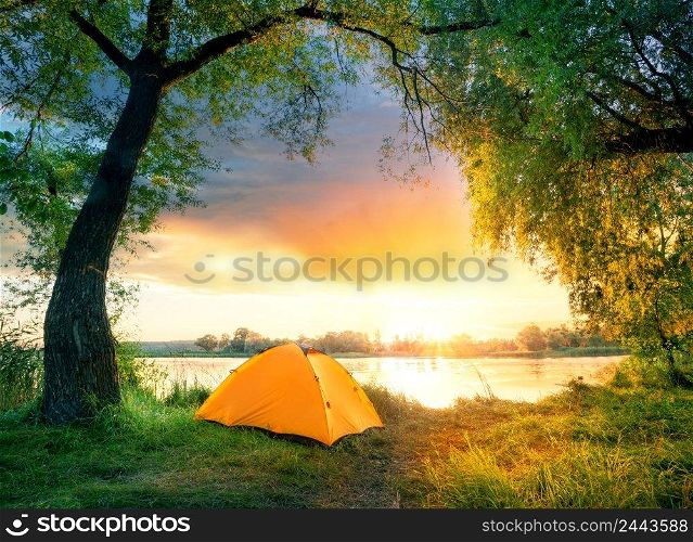 Orange tent surrounded by green leaves by the river. Orange tent surrounded by green leaves by river