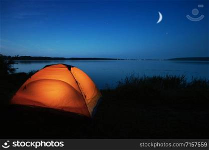 Orange tourist tent lit by a lake. Night sky. The concept of privacy, travel and harmony. Orange tourist tent lit by a lake