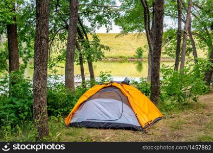 Orange touristic tent near lake in forest at sunrise. Touristic tent in forest