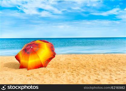 Orange umbrella on golden sand beach in a sunny day, blue sea in background