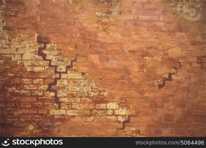 Orange wall in grunge look with peeling paint an an old brick house