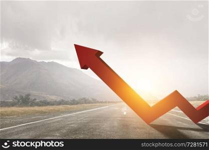 Orange zigzag increasing arrow standing on highway against mountain landscape and cloudy sky background. Orange zigzag increasing arrow standing on highway against mountain landscape background