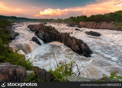 Oranges and yellows glowing off of tall summer storm clouds around sunset at Great Falls Park in Virginia.