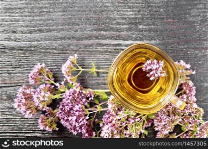 Oregano herbal tea in a glass cup, fresh pink marjoram flowers on wooden board background from above