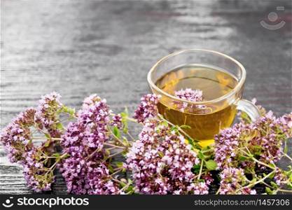 Oregano herbal tea in a glass cup, fresh pink marjoram flowers on wooden board background