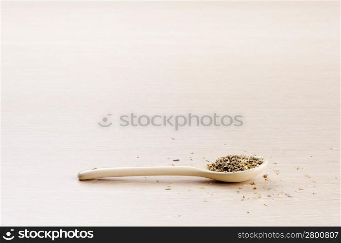 Oregano in a spoon with some spilt over the wooden background