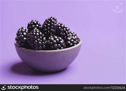 Organic blackberries in a bowl, isolated on a purple background. Close-up of fresh blackberries fruits. Ripe berries bowl. Summer sweet fruits.